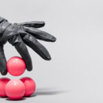 Mano con guanto nero che tiene palline vaginali rosse per esercizi di Kegel